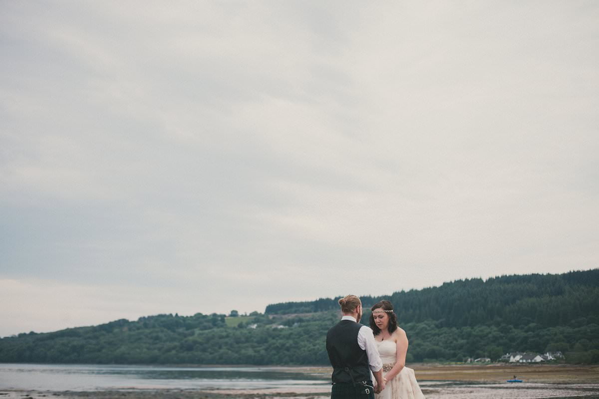 Bride and groom hold hands by sea during first look at wedding elopement outside Glenisle Hotel on The Isle of Arran Scotland